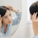 鏡を見て白髪に悩む50代の女性