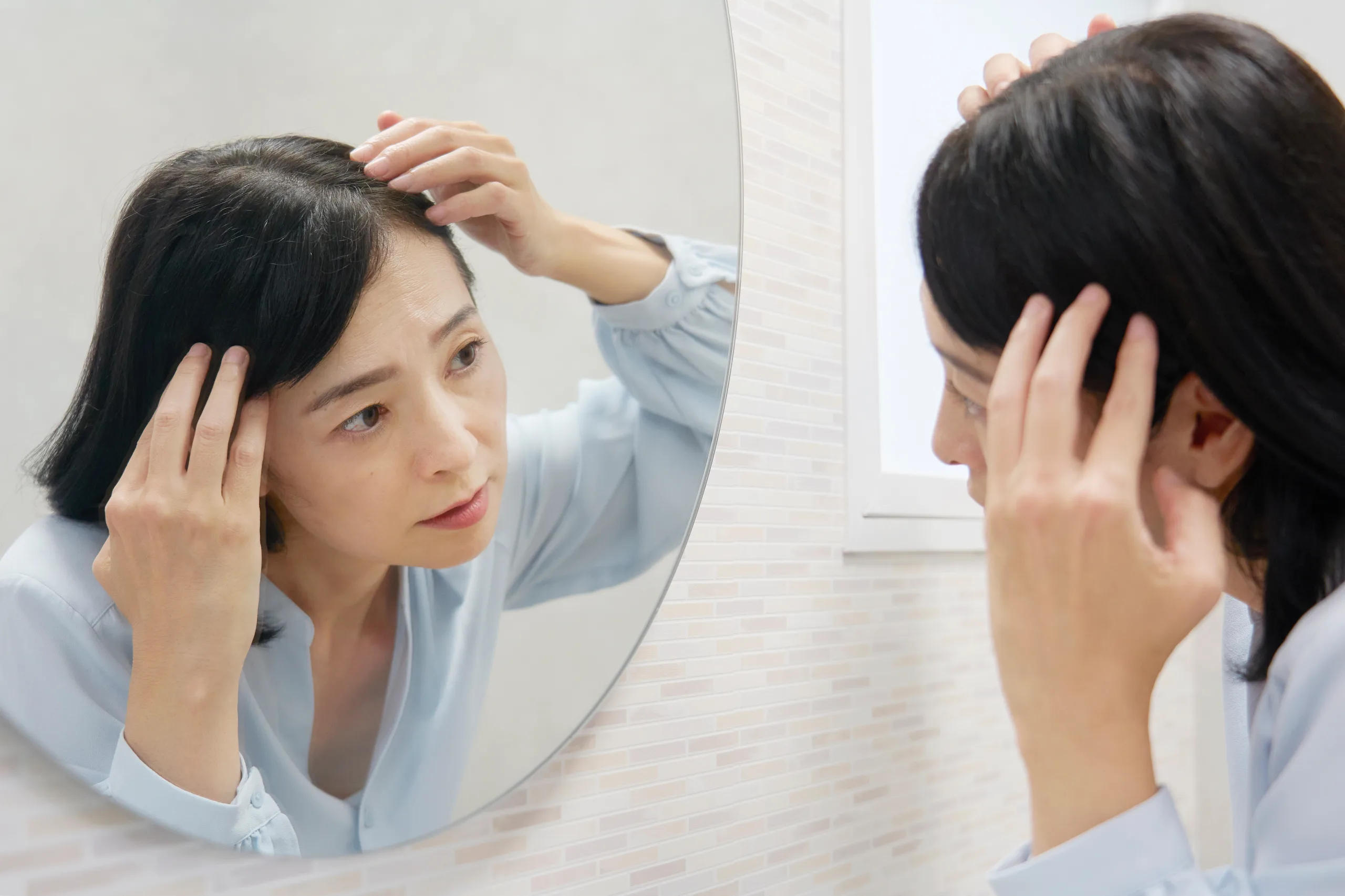 鏡を見て白髪に悩む50代の女性
