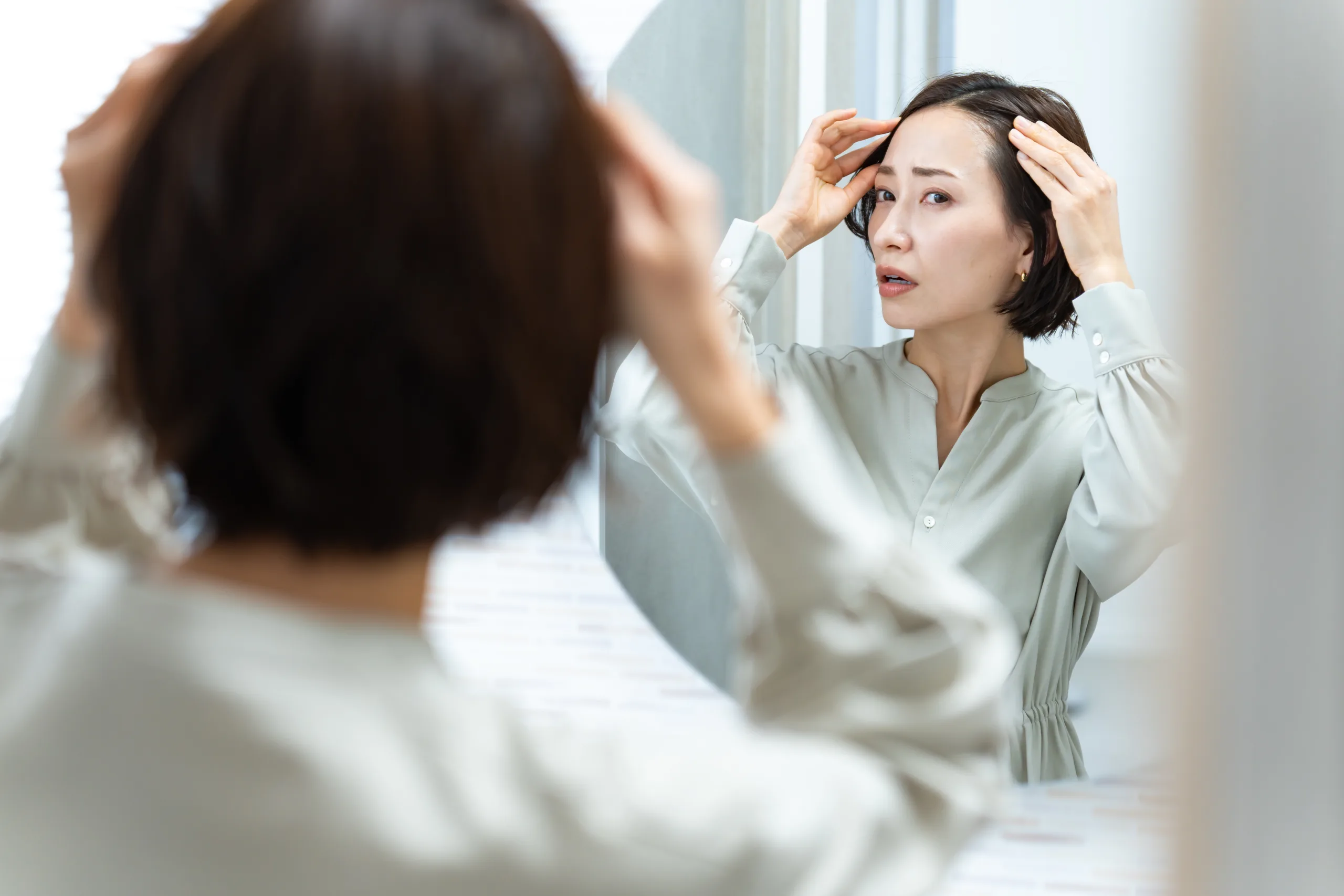 鏡を見て髪の毛を気にする日本人女性